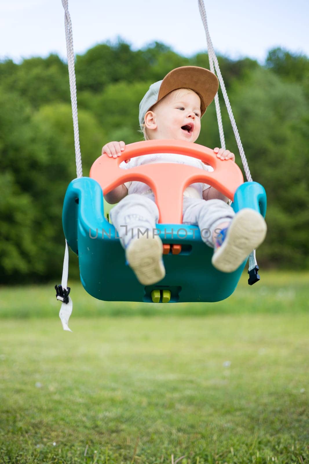Adorable little happy Caucasian infant baby boy child swinging on playground outdoors. by kasto