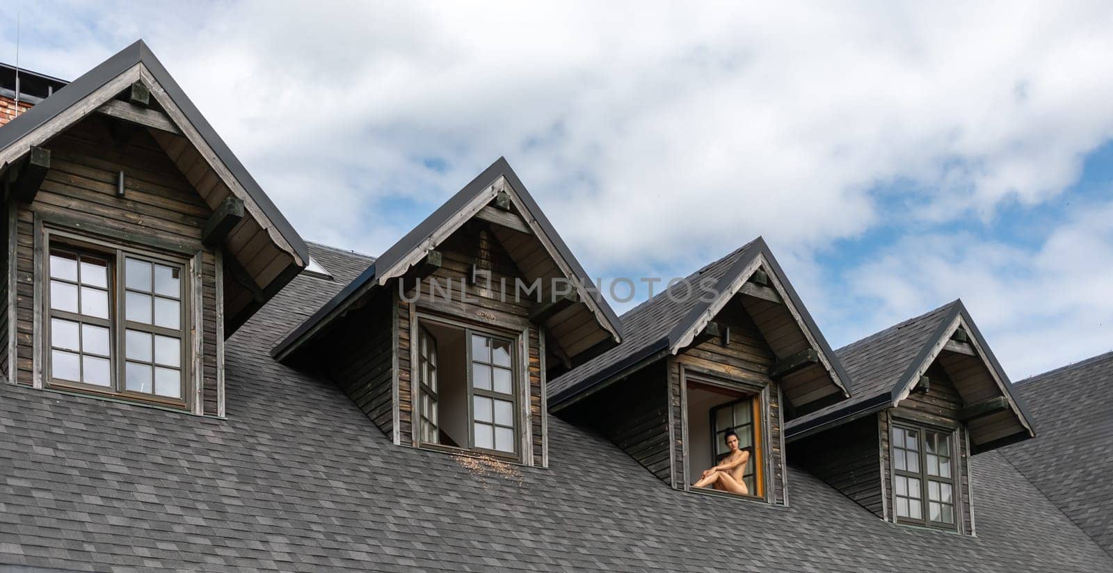 A young nude woman sits in the window opening of a country house enjoying a beautiful summer day