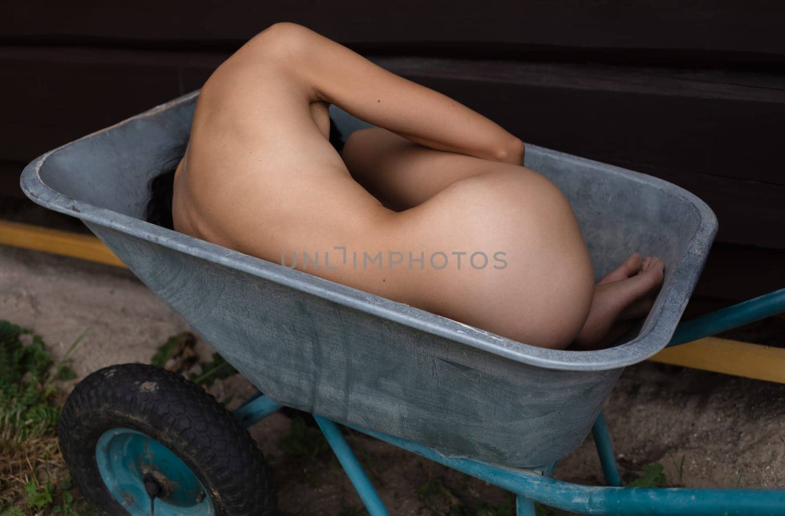 Young nude woman posing lying in a construction wheelbarrow at a country house construction site