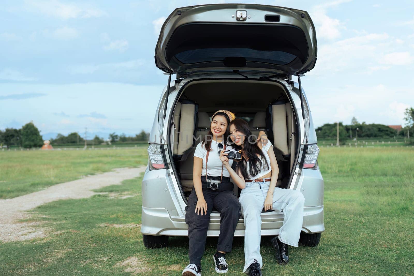 Two women friends and open trunk of car to sit back and relax after reaching rest place by itchaznong