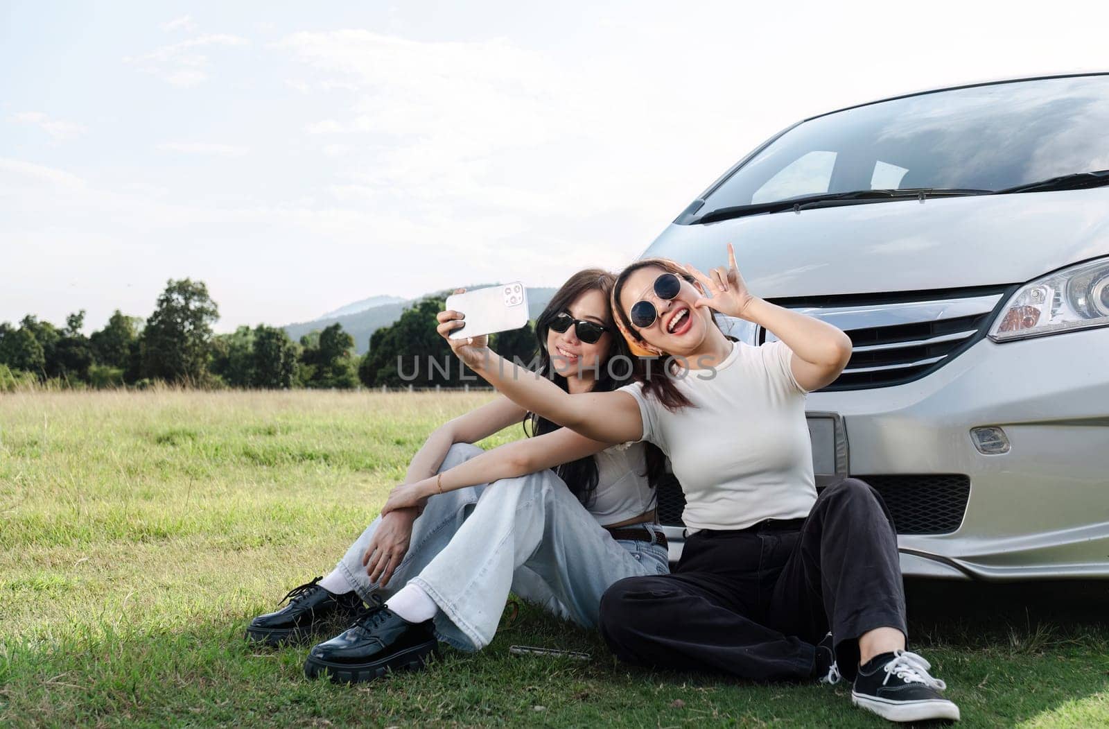 Two young women in white t-shirts and jeans sit back and relax, taking selfies together with their cell phones..