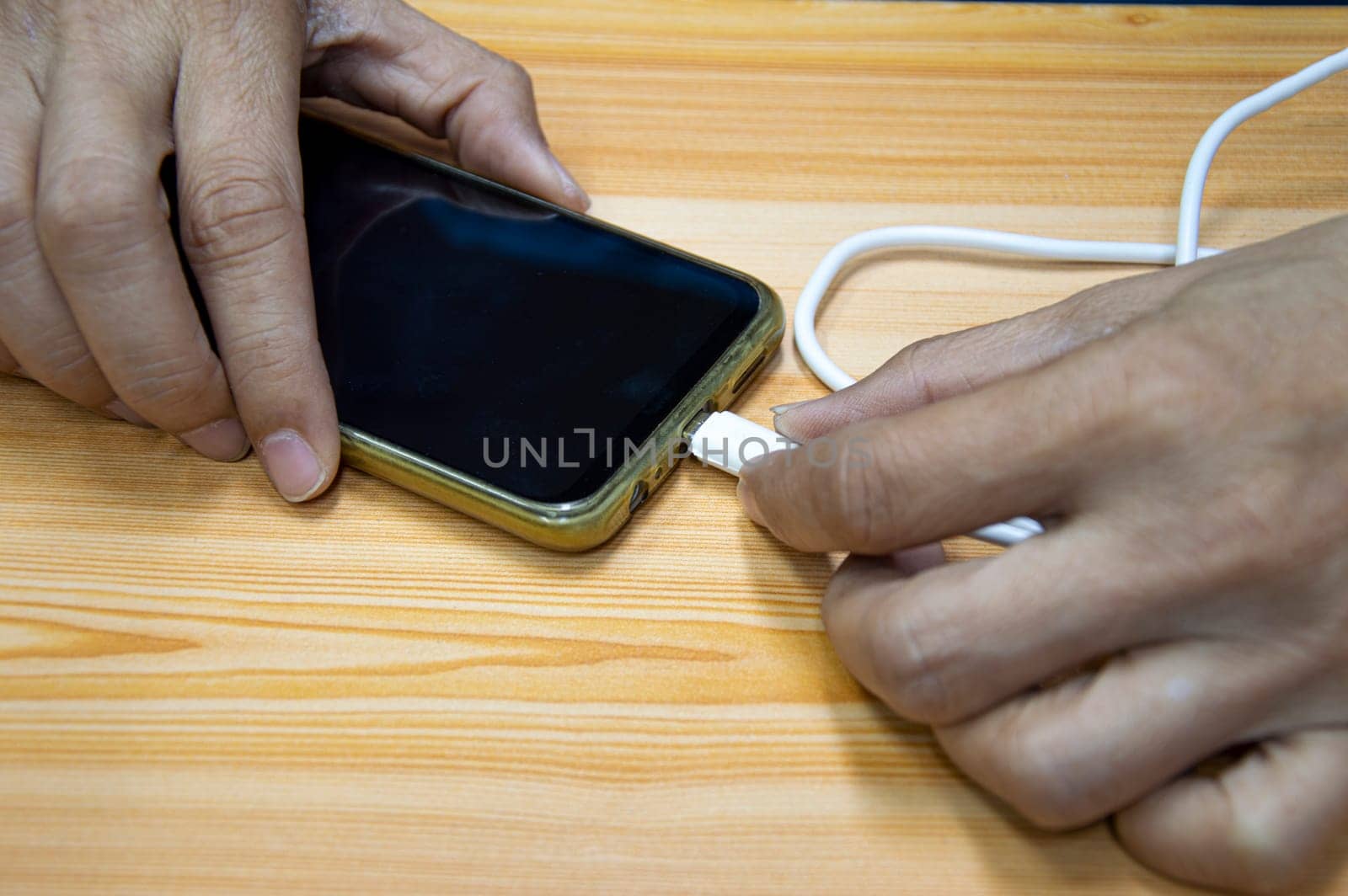 Top view. Male hand plugging in the battery charger of a smartphone. by boonruen