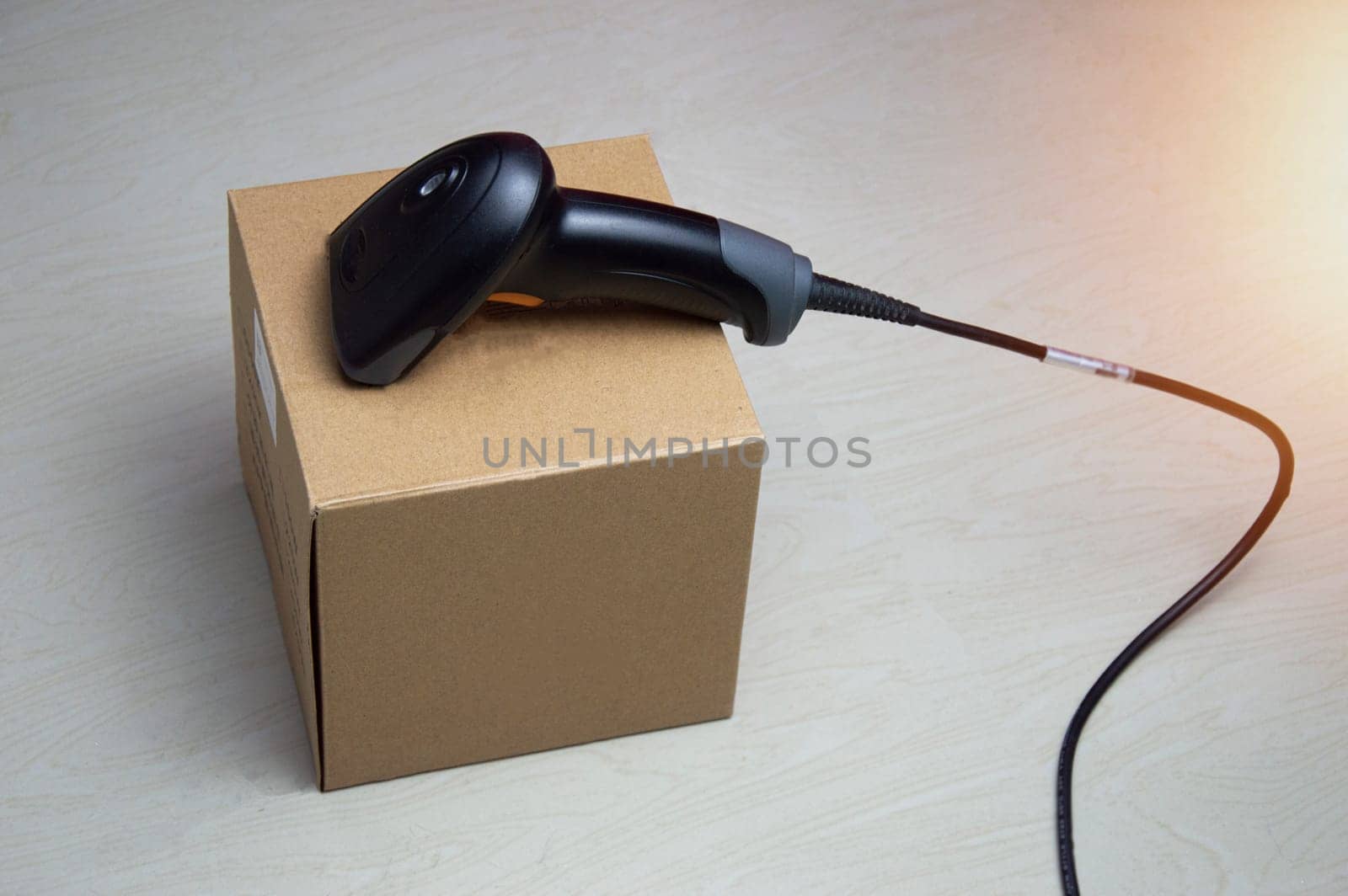 A barcode scanner is placed on a brown box.