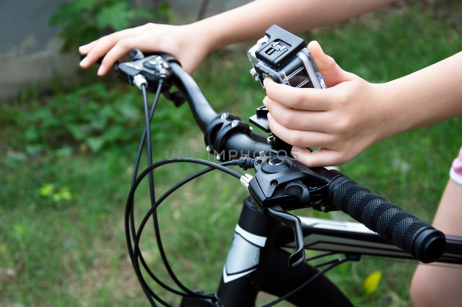 A woman's hand adjusts a digital camera mounted on the handlebars of a mountain bike.