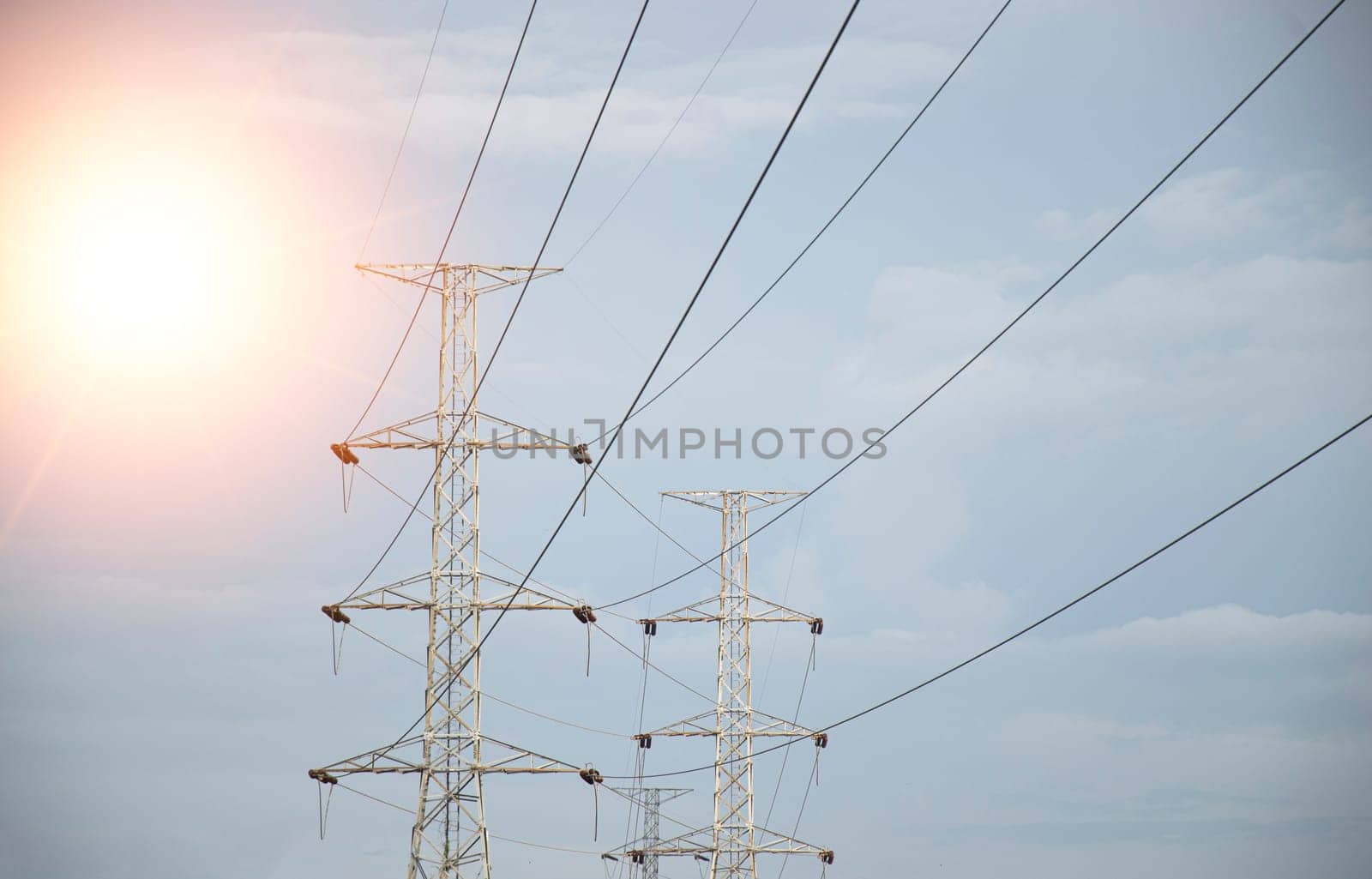 High voltage towers at sunset background. Power lines against the sky by boonruen