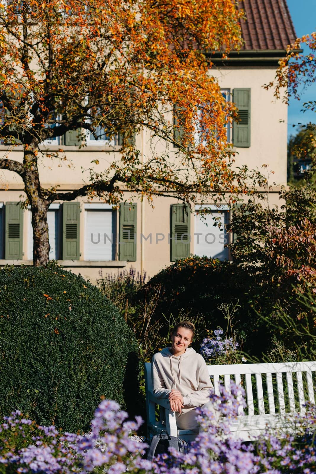 a girl sits on a bench in the park and enjoys the sun. Portrait young adult attractive woman enjoy sitting on bench and relaxing calm carefree rest in city park against green grass and trees on sunny day. Single female person relaxing chilling outdoors