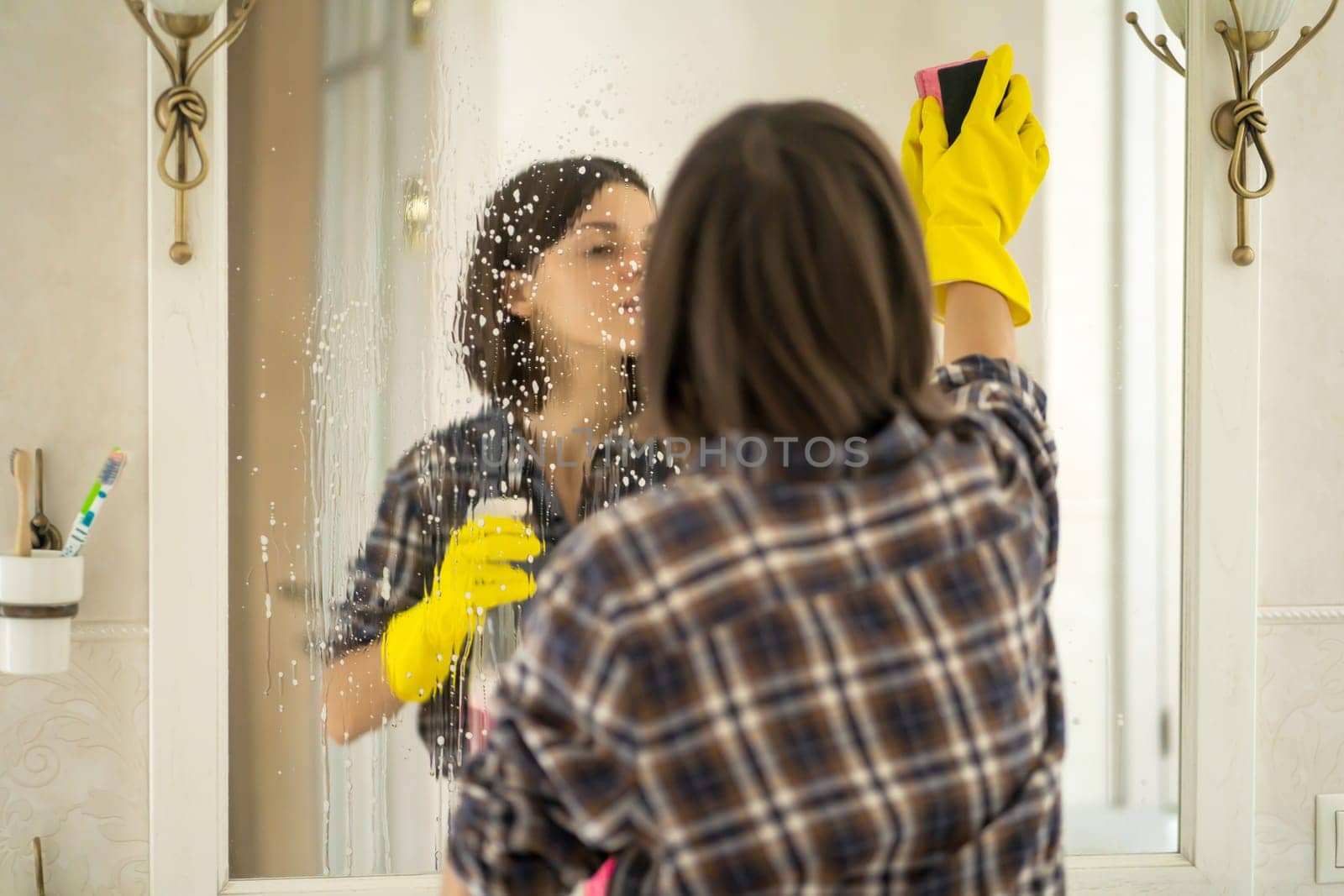 Young woman is washing mirror in the bathrom. by africapink