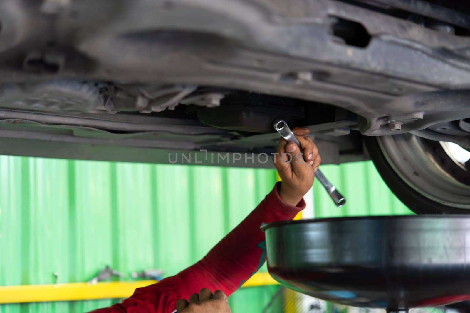 Car mechanic drain the old lubricant engine oil at car garage for changing the oil in a car engine