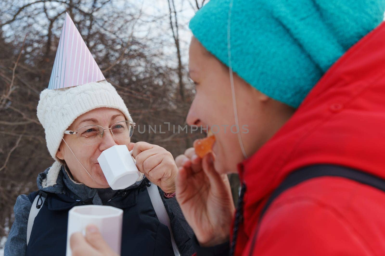 Celebrating friendship in a snowy forest with warm drinks and playful hats during a winter gathering