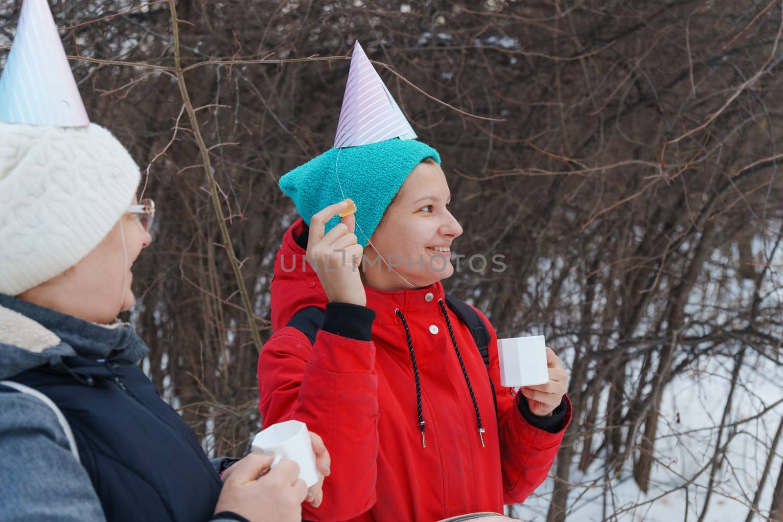 Two friends savoring warm beverages while chatting in a snowy forest.