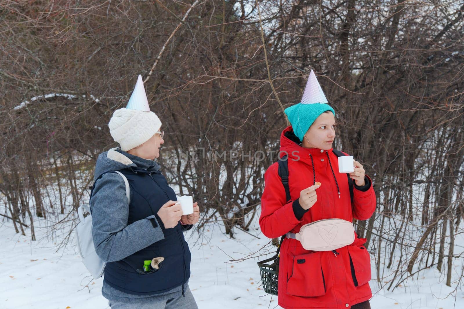 Two friends savoring warm beverages while chatting in a snowy forest.