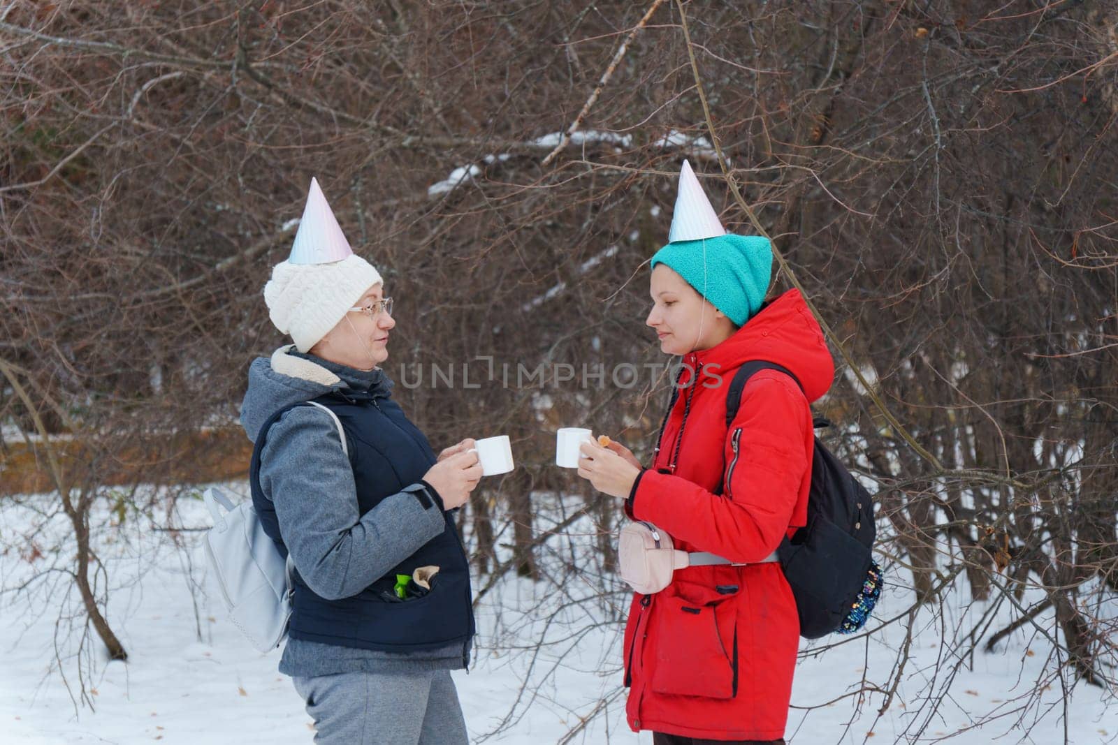 Two friends savoring warm beverages while chatting in a snowy forest.