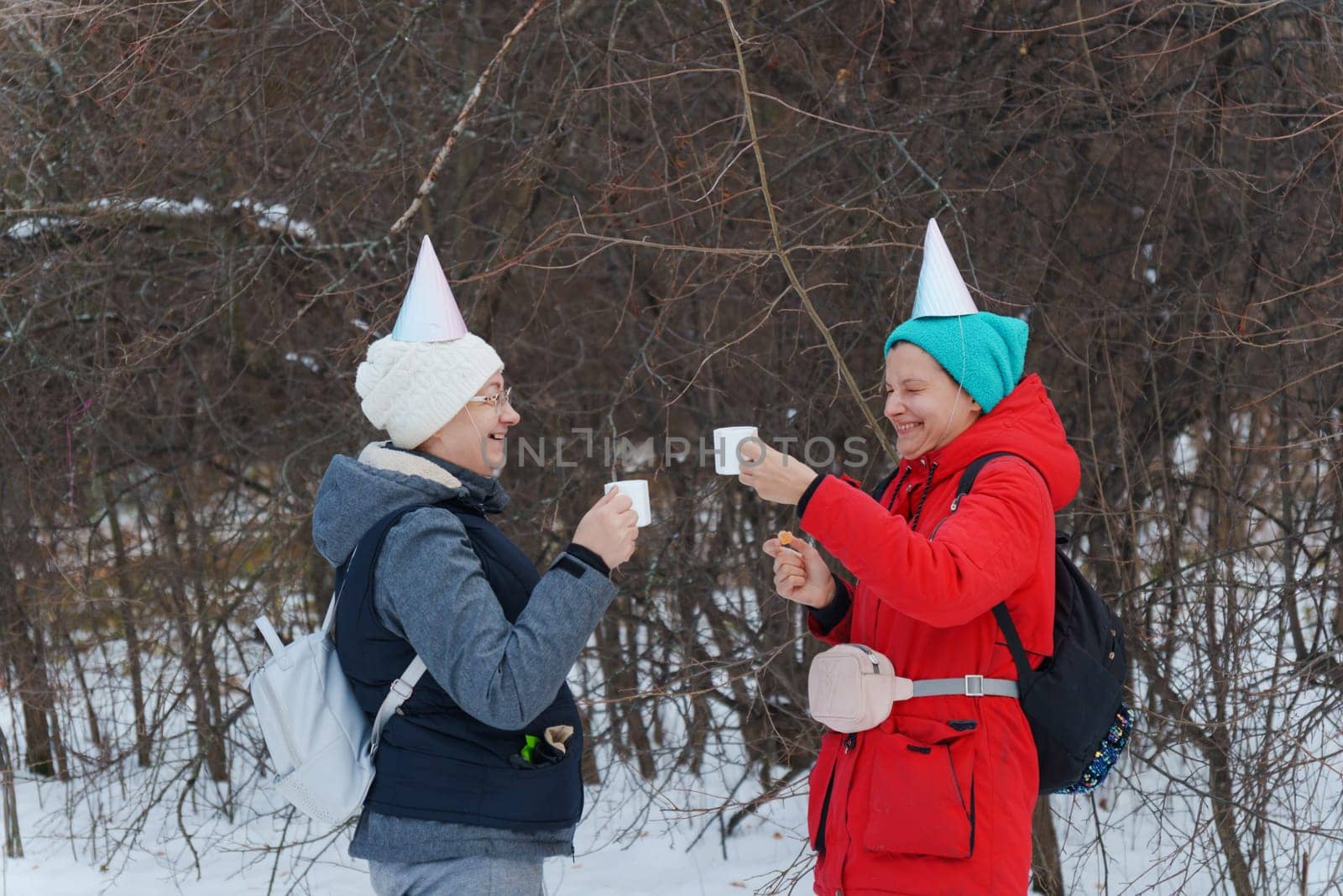 Two friends savoring warm beverages while chatting in a snowy forest.