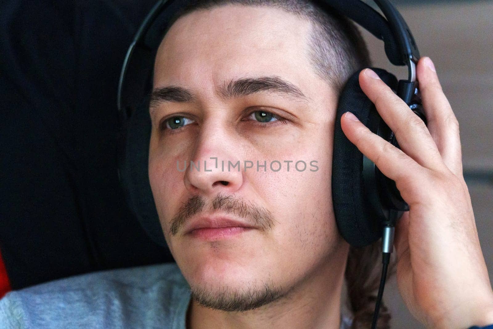 A thoughtful young man listens to music with headphones, his expression reflecting admiration and focus.