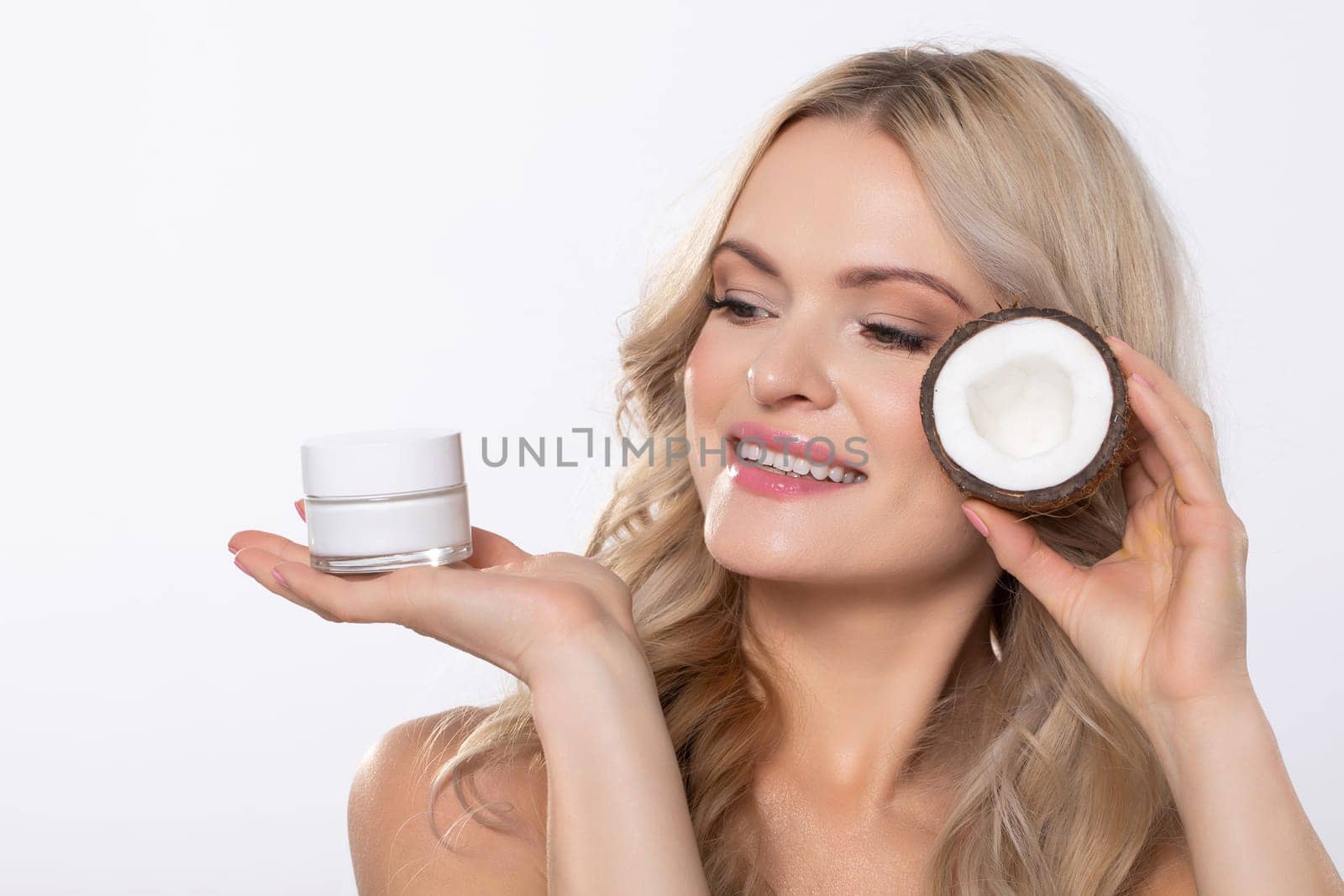 A beaming and smiling woman enthusiastically showcasing various skincare products to achieve a radiant complexion
