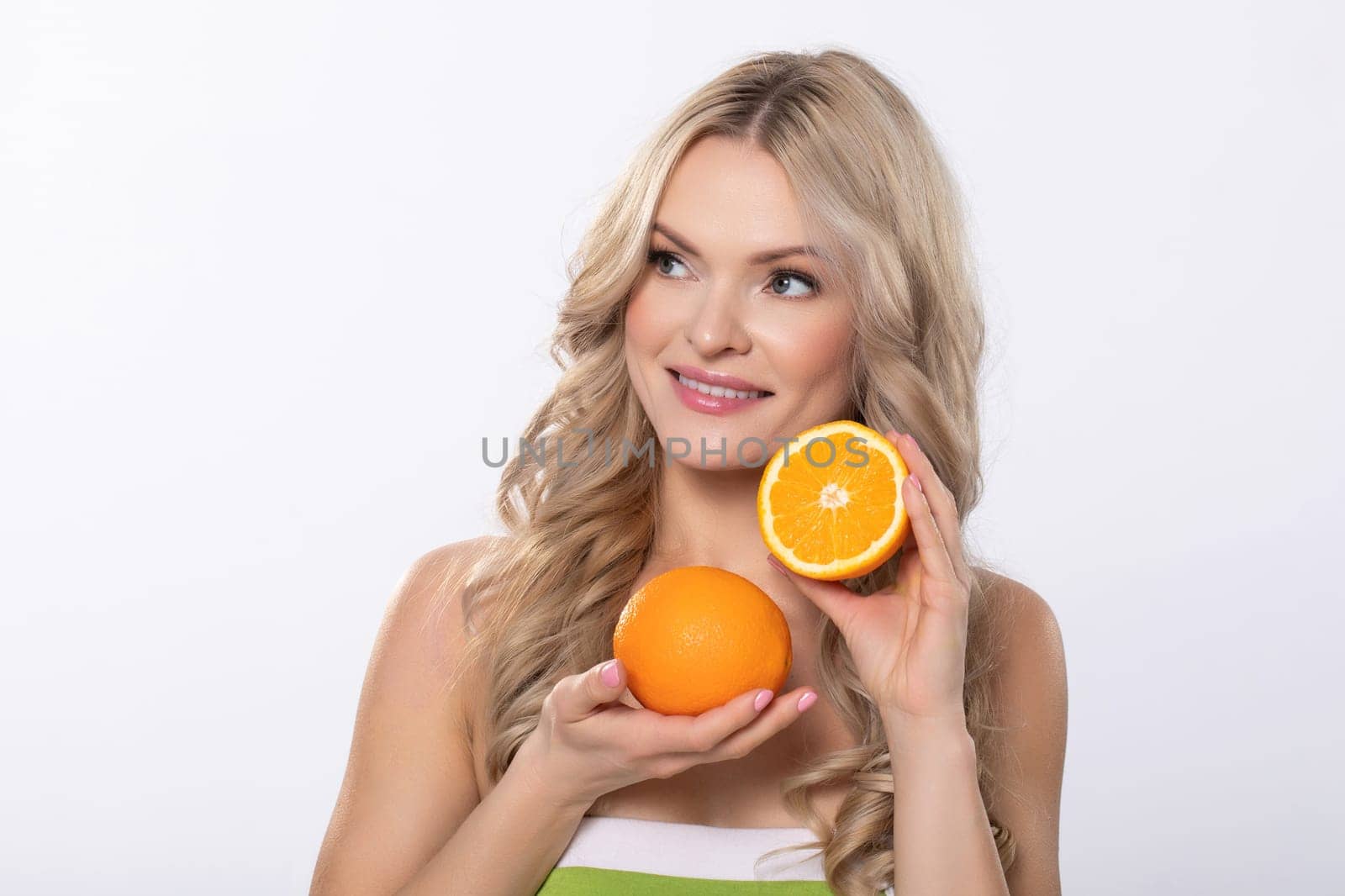 A vibrant woman joyfully shows a bright orange fruit, highlighting the importance of health and freshness