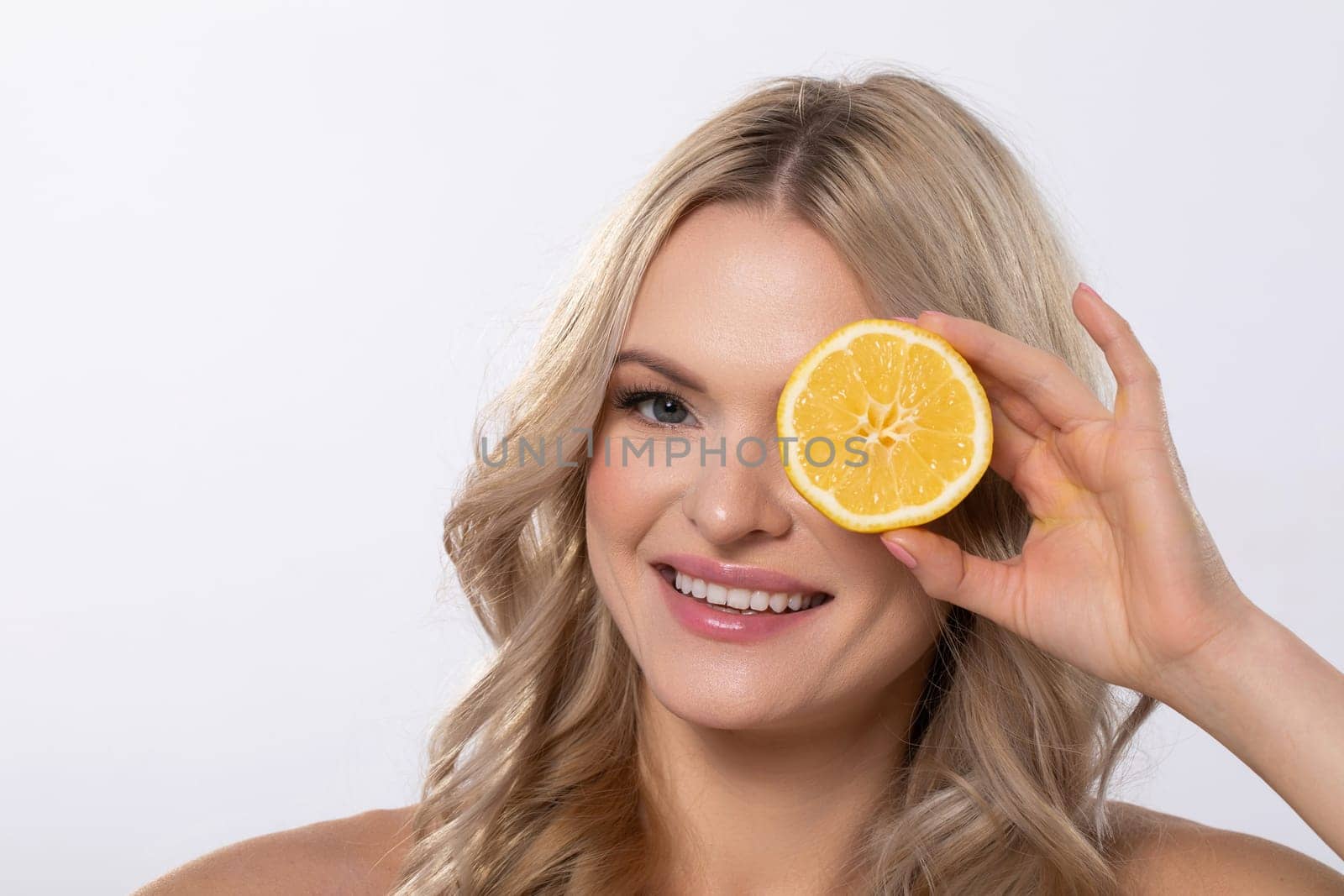 A joyful woman playfully holds a lemon slice to her face, showcasing the delightful essence of freshness and health