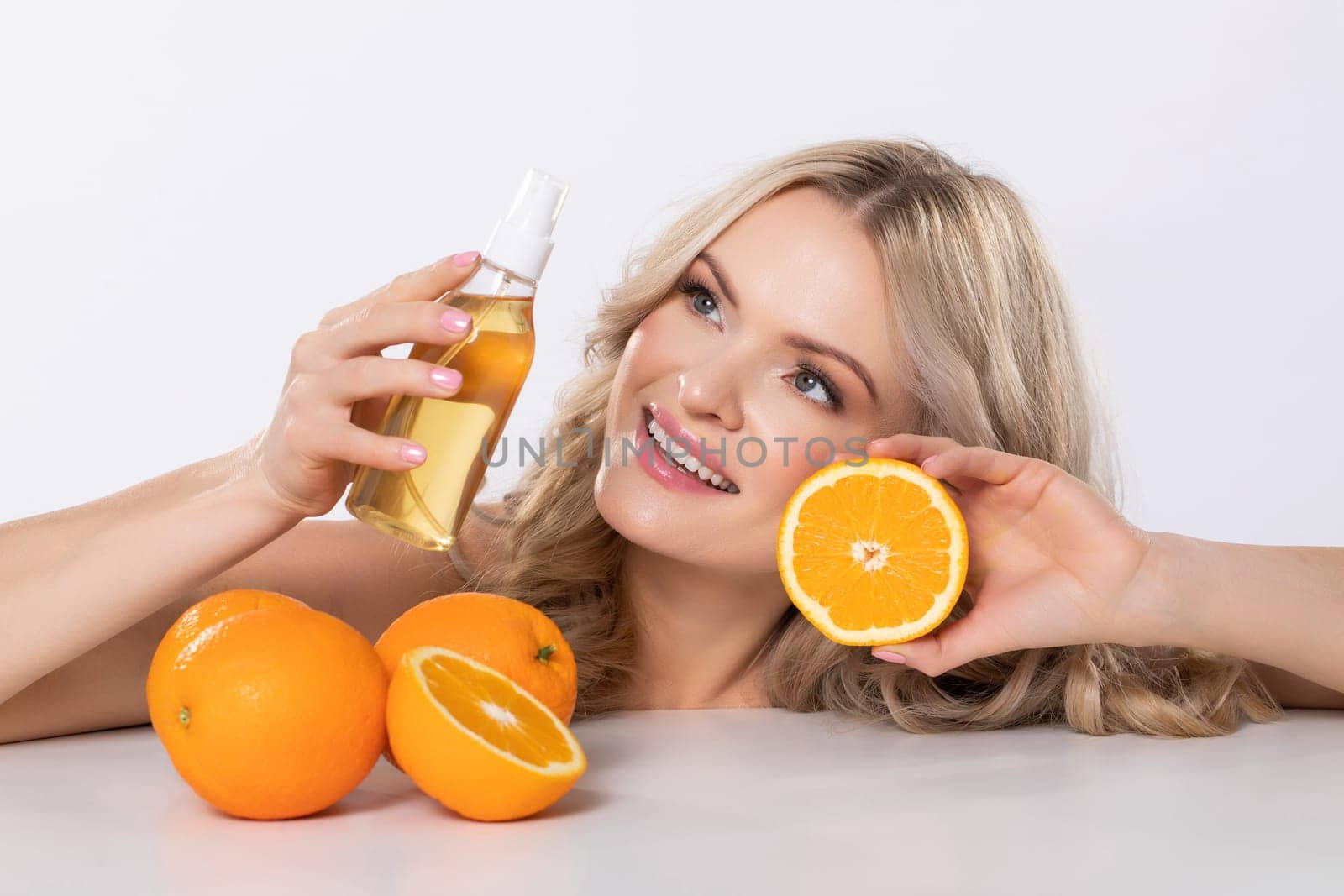 A radiant woman showcases orange skincare products and fresh oranges, highlighting wellness and natural beauty