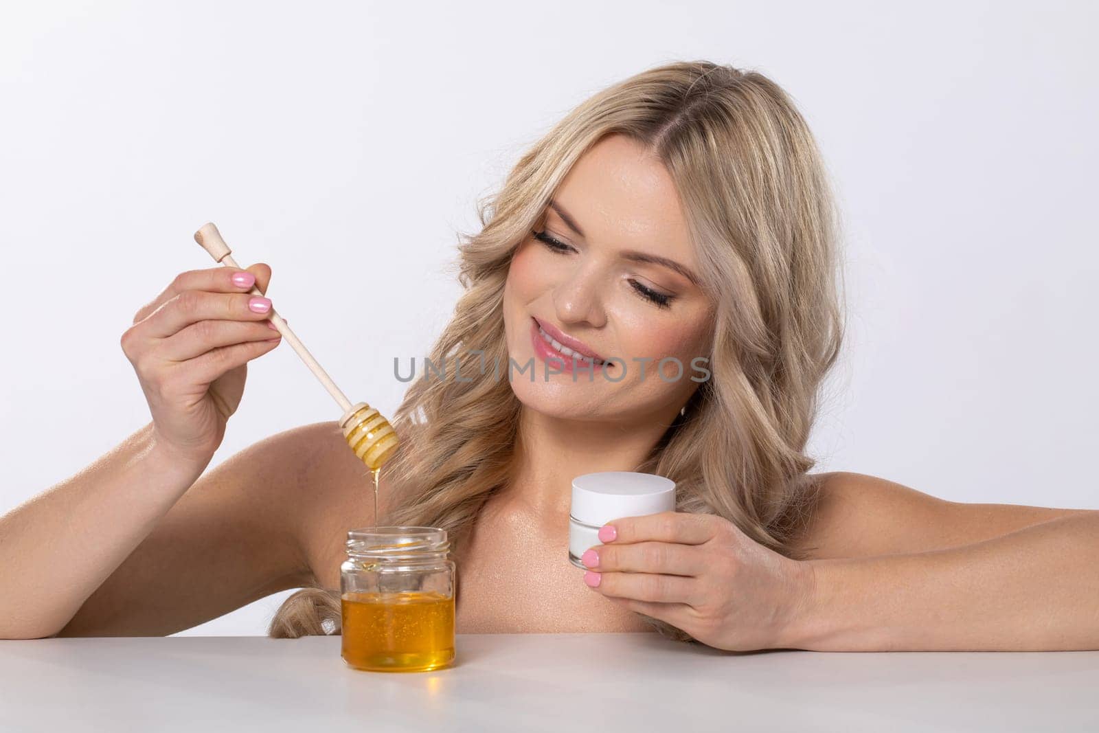 A joyful woman happily indulging in her skincare routine while using honey and a luxurious cream product