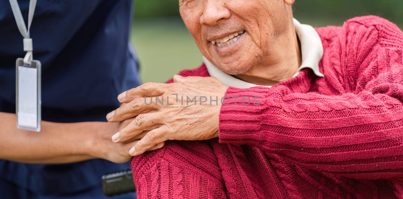 A heartwarming close-up of an elderly man's smiling face while a caregiver's hand rests on his shoulder, showcasing compassion in a beautiful garden setting.