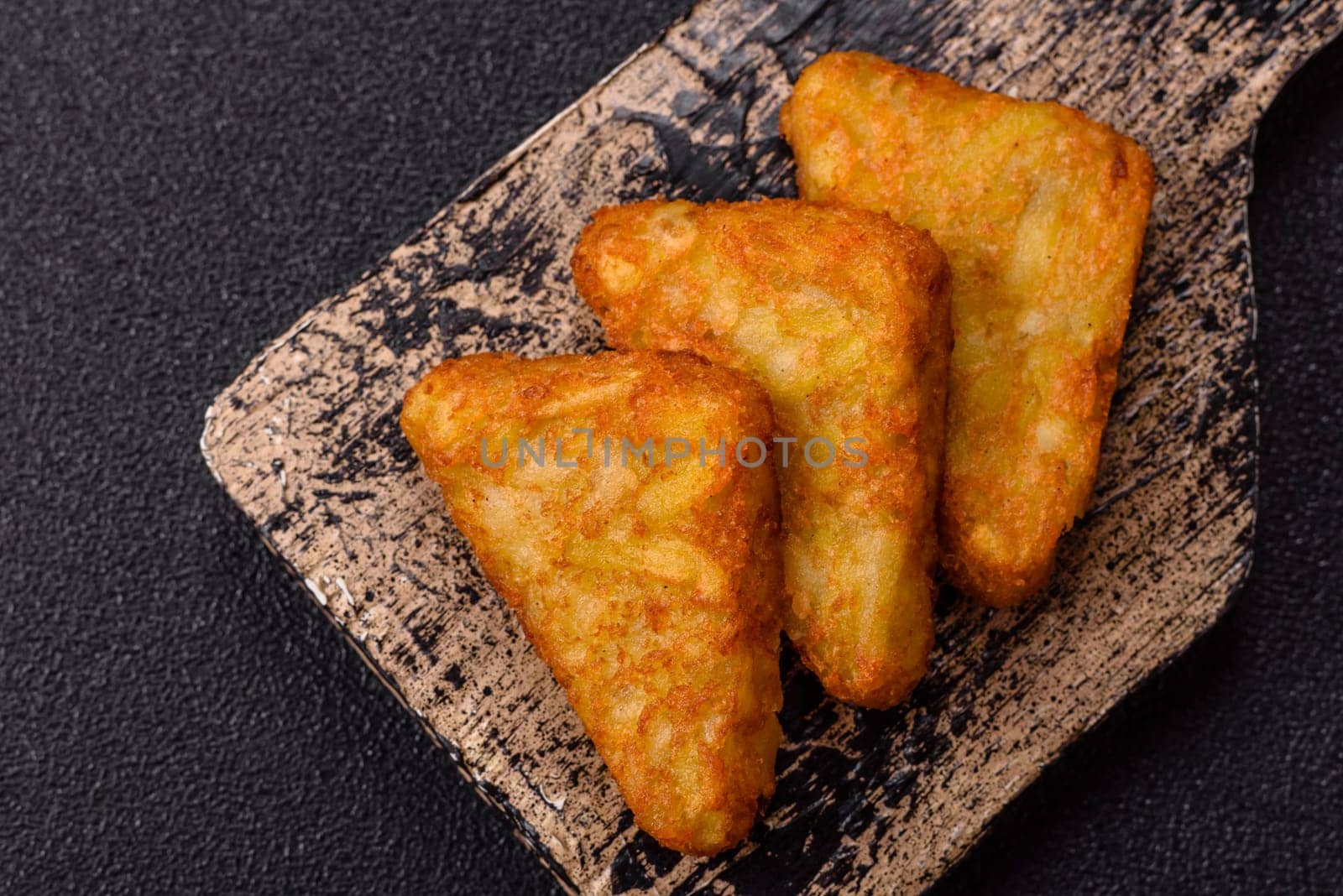 Hash browns with potatoes and onions, salt and spices on a dark concrete background