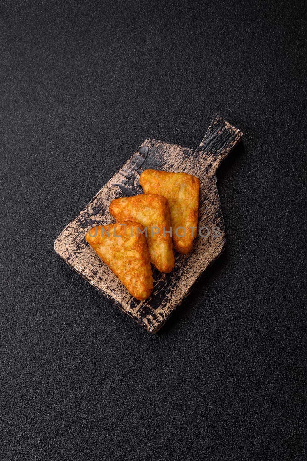 Hash browns with potatoes and onions, salt and spices on a dark concrete background