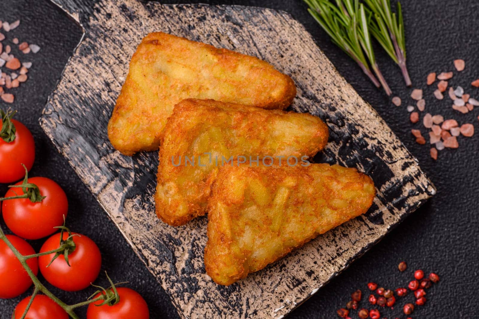 Hash browns with potatoes and onions, salt and spices on a dark concrete background