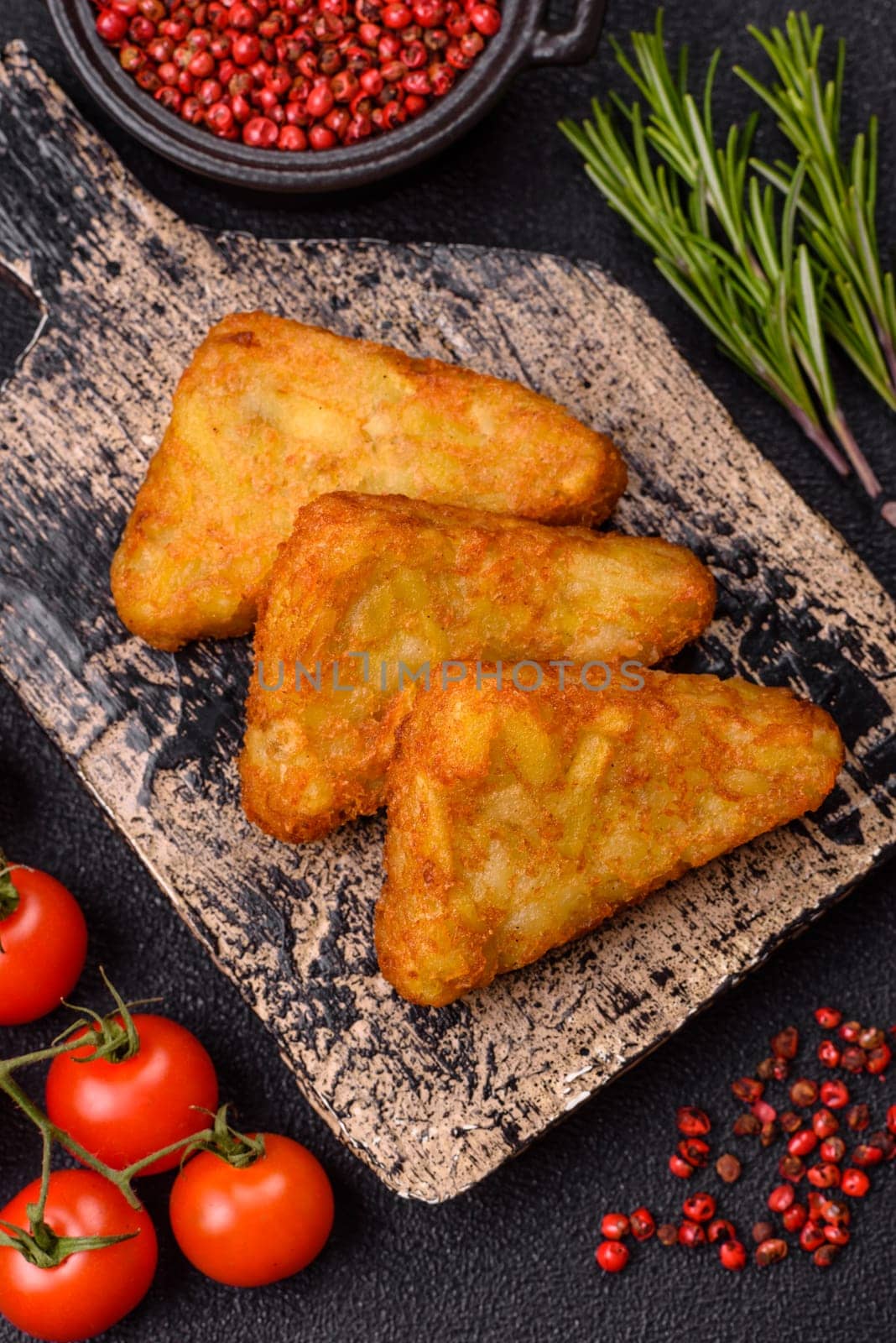 Hash browns with potatoes and onions, salt and spices on a dark concrete background