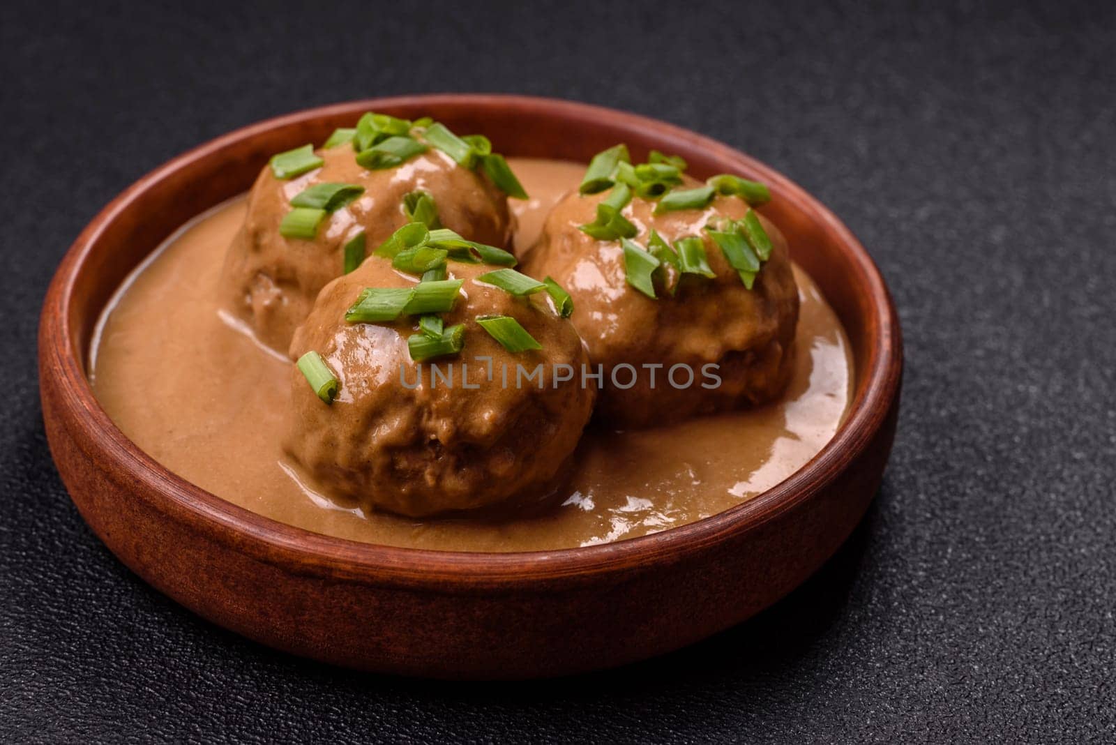 Meatballs with salt and spices in creamy caramel sauce on a dark concrete background
