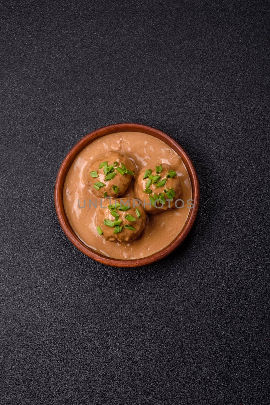 Meatballs with salt and spices in creamy caramel sauce on a dark concrete background