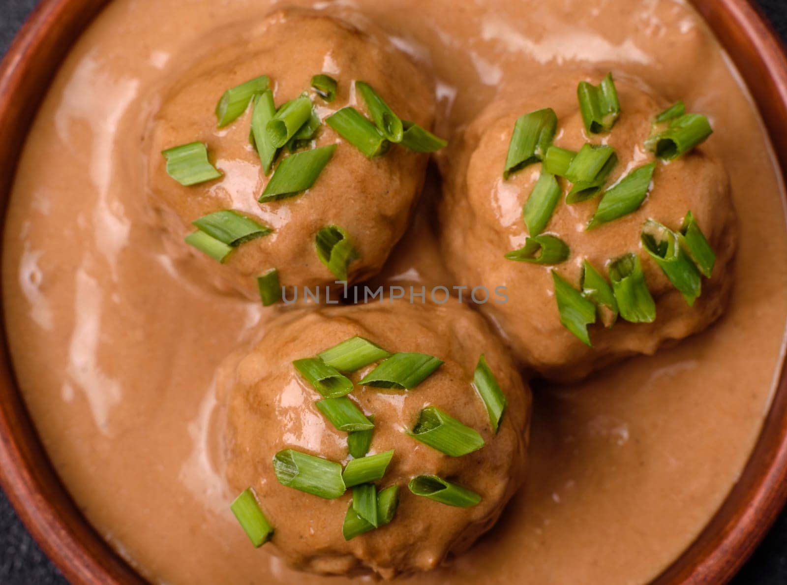 Meatballs with salt and spices in creamy caramel sauce on a dark concrete background
