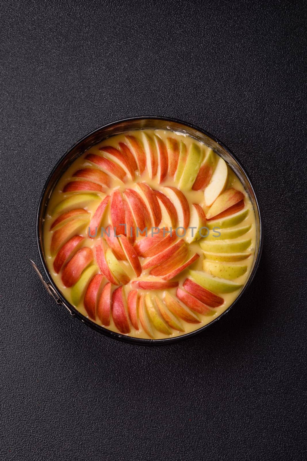 Raw sweet apple pie in a mold prepared for baking on a dark concrete background