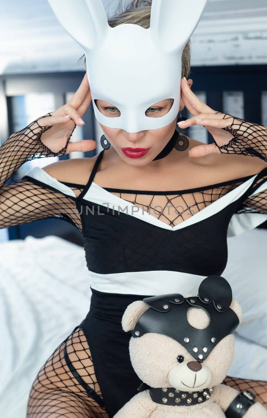 Sexy girl in a black dress and a white rabbit mask from a sex shop poses erotically seducing on the bed