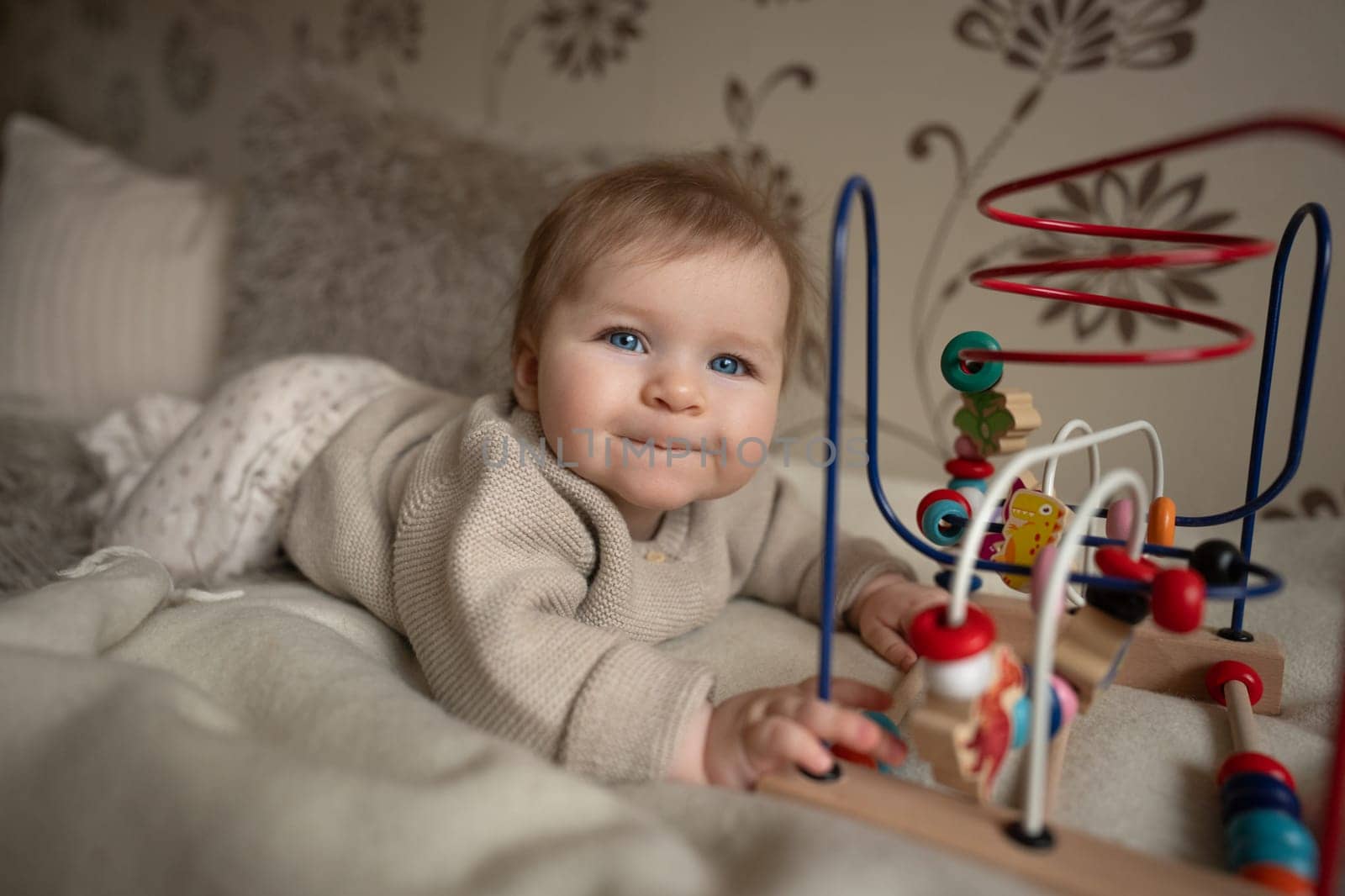 Adorable 6-month baby playing with educational toy on bed coat. Activity for motor and sensory development. High quality photo