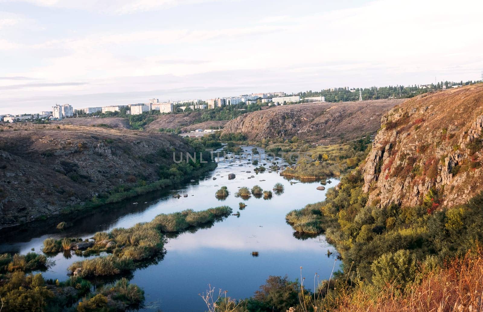 A huge wide river flows between steep banks. A city is visible on the horizon. Autumn forest on the banks of the river. Cliffs of granite stones. Bushes grow in the middle of the river. southern bug