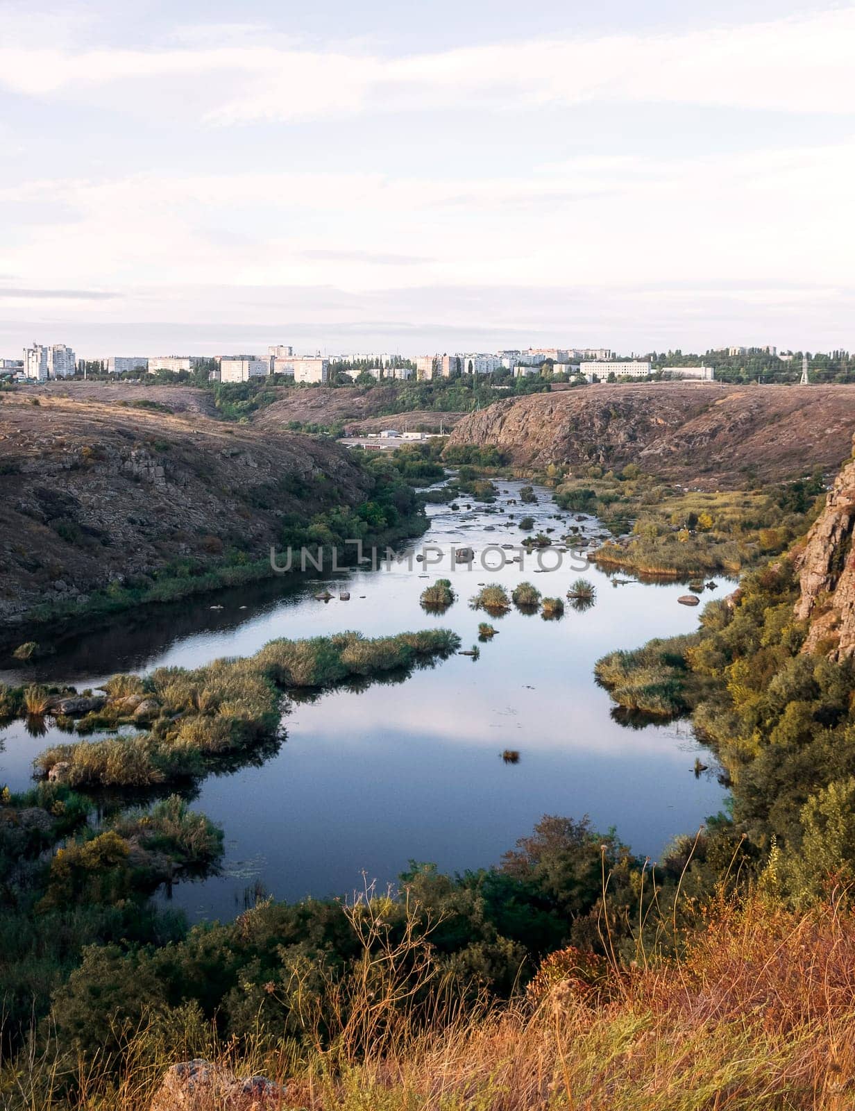 A huge wide river flows between steep banks. A city is visible on the horizon. Autumn forest on the banks of the river. Cliffs of granite stones, Bushes grow in the middle of the river. southern bug