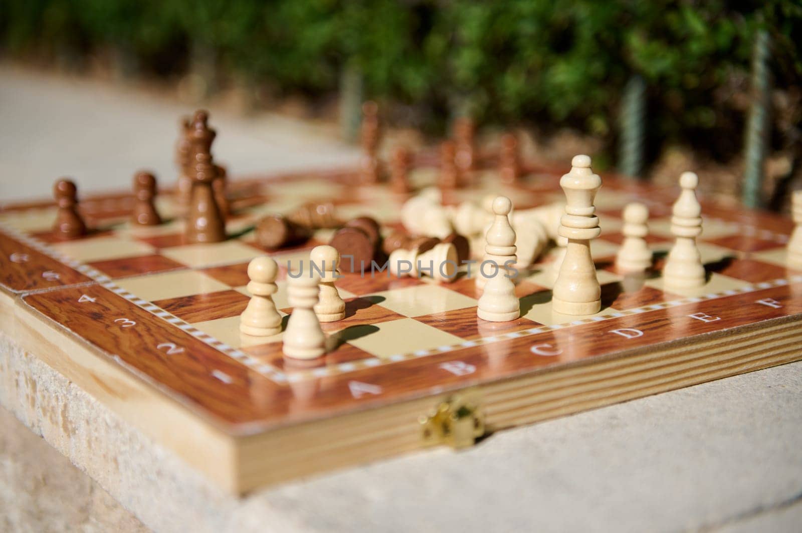 A close-up outdoor photograph featuring a wooden chessboard with scattered chess pieces.