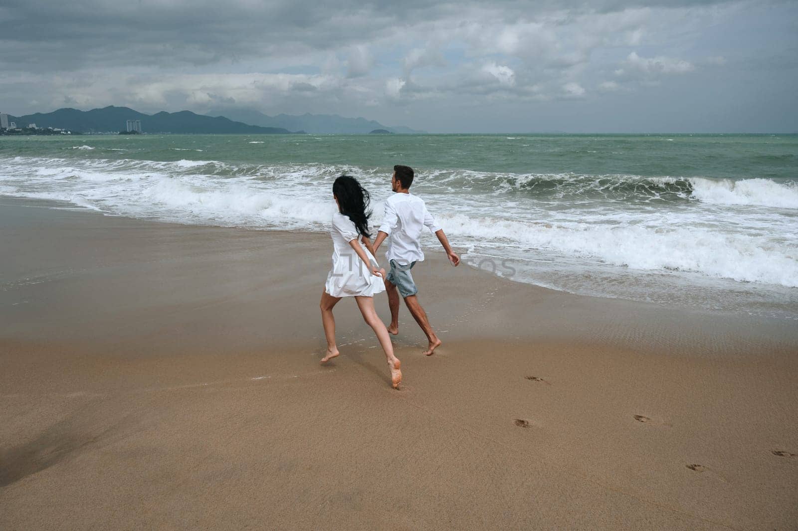 back of couple in love runs along the beach by the sea in summer on vacation