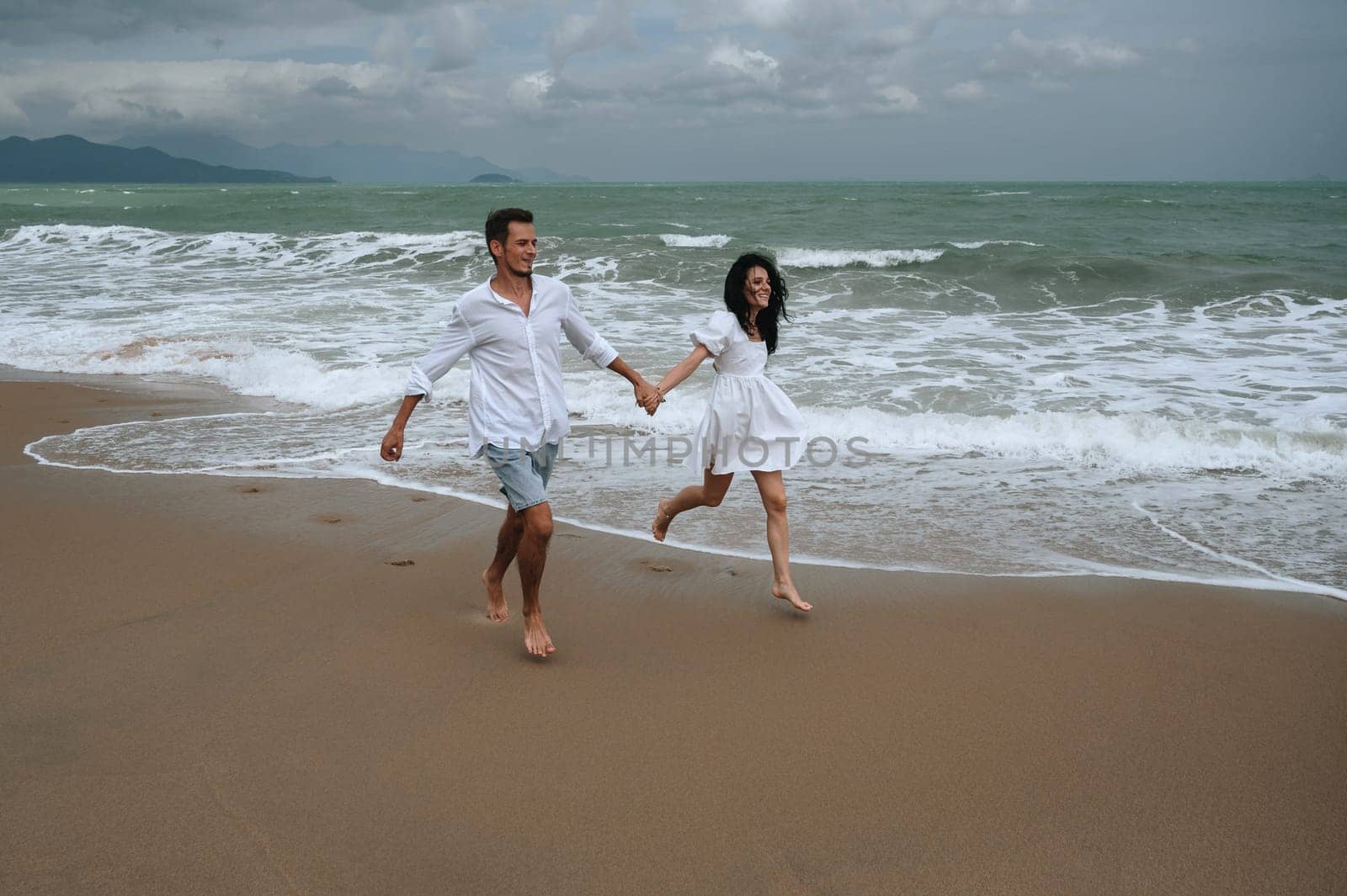 beautiful young couple in love runs along the beach by the sea in summer on vacation