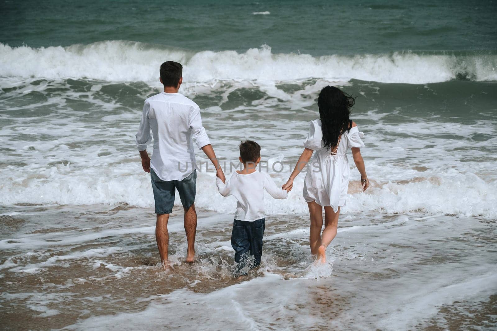 back of family parents with a child boy son on the beach in the sea on summer vacation