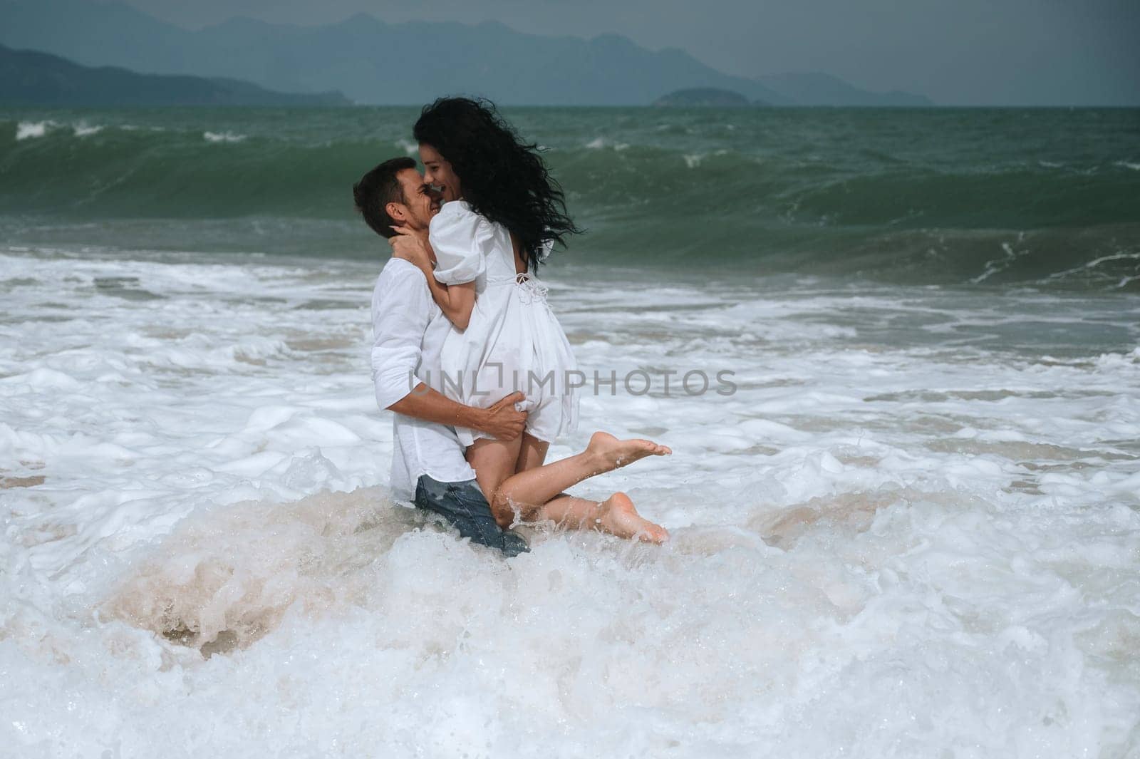Happy young beautiful couple in love hugging in the water on the beach by the sea in summer on vacation