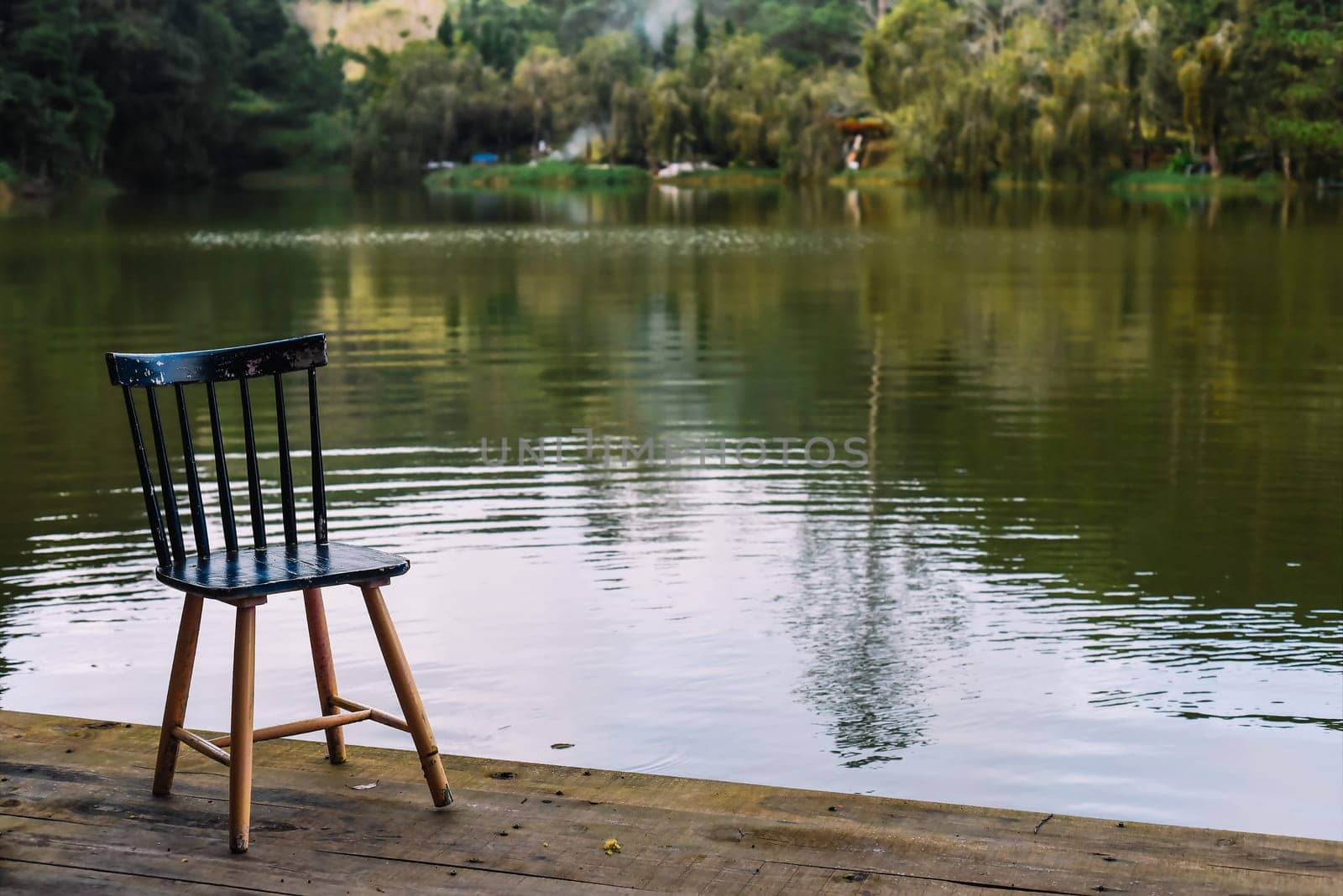 Depressive dark concept of loneliness with showing empty chair near lake and forest in the evening