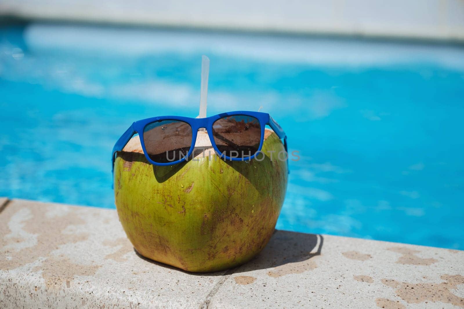 drinking coconut with a straw in sunglasses relax by the swimming pool at the resort in the hotel in summer
