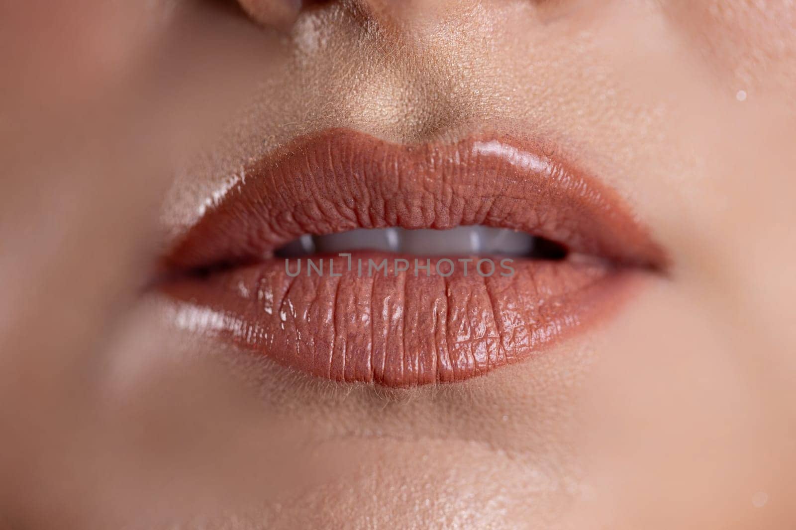 A stunning closeup image highlighting glossy, beautiful lips that showcase a popular, trendy nude lip color and shine