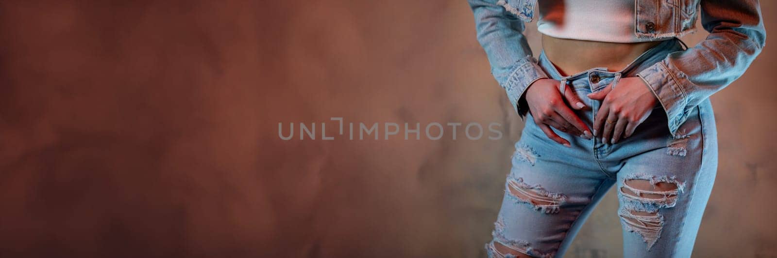 A stylish woman is showcasing her trendy distressed jeans and a cropped jacket against a striking textured backdrop