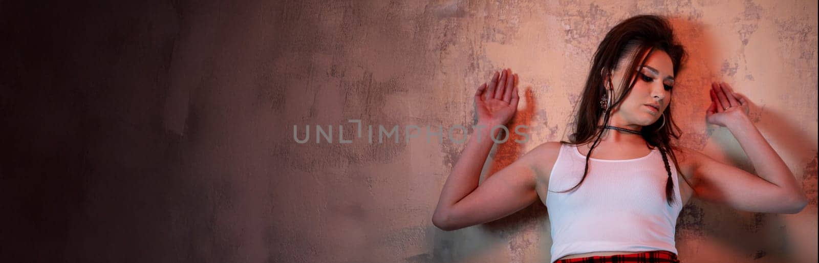 A young woman in casual attire poses gracefully against a textured wall, showcasing fashion and mood.