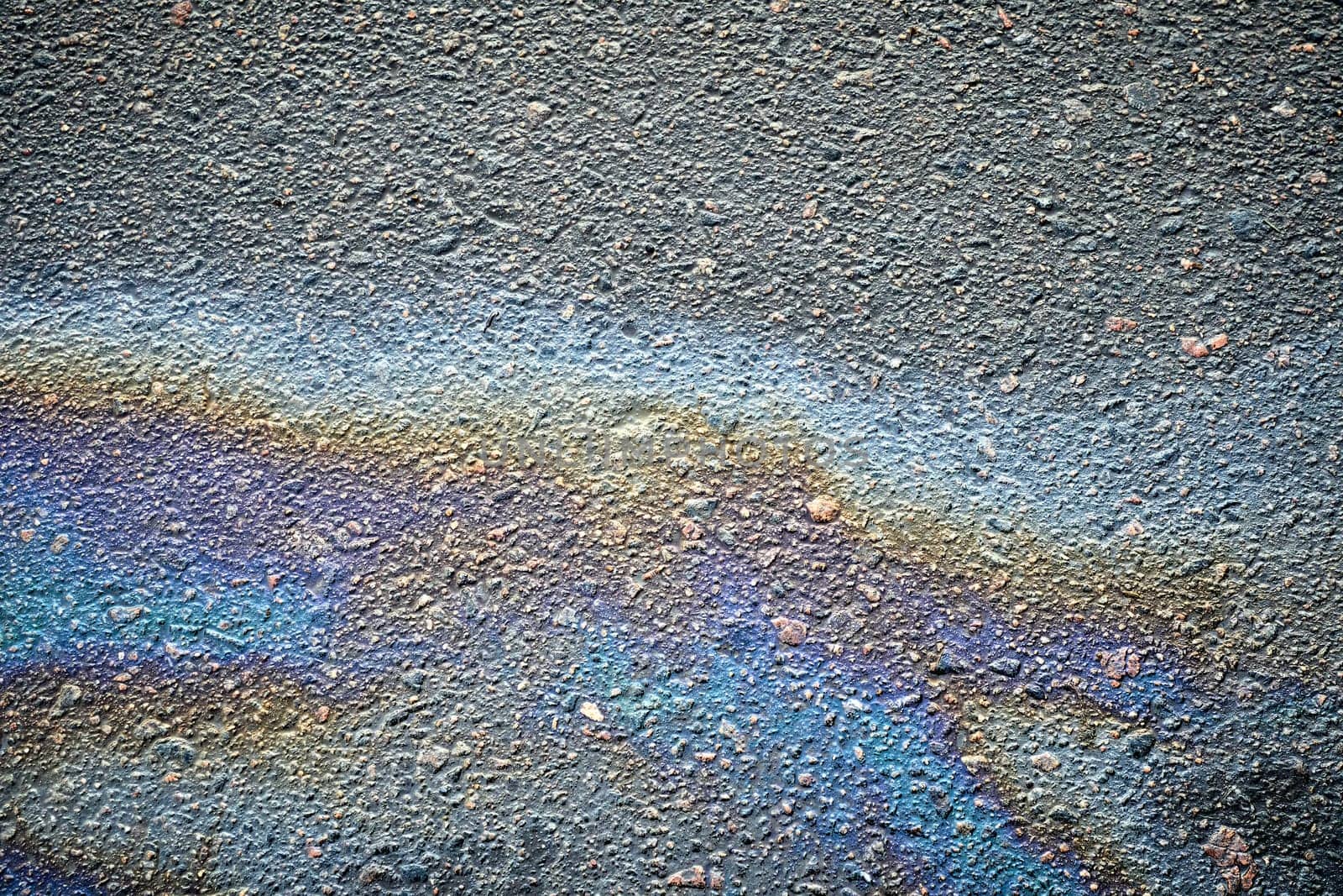 Gasoline or oil spill generates vibrant patterns on the asphalt road, signaling environmental pollution and potential road hazards.