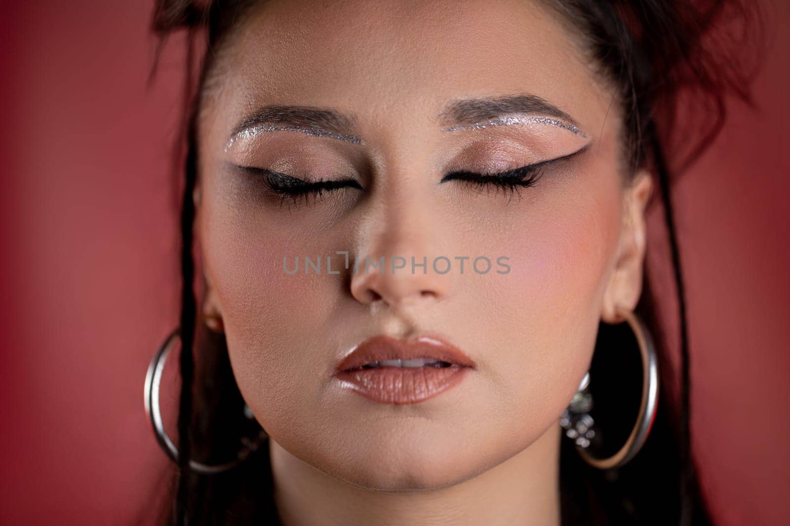 A stunning portrait features glittery makeup and chic earrings against a vibrant, colorful background