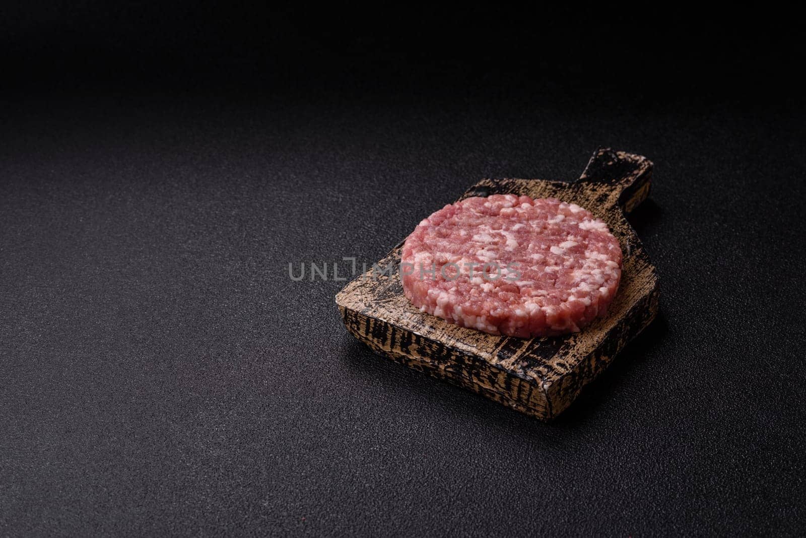 Fresh raw ground beef or pork burger patty with salt and spices on textured concrete background
