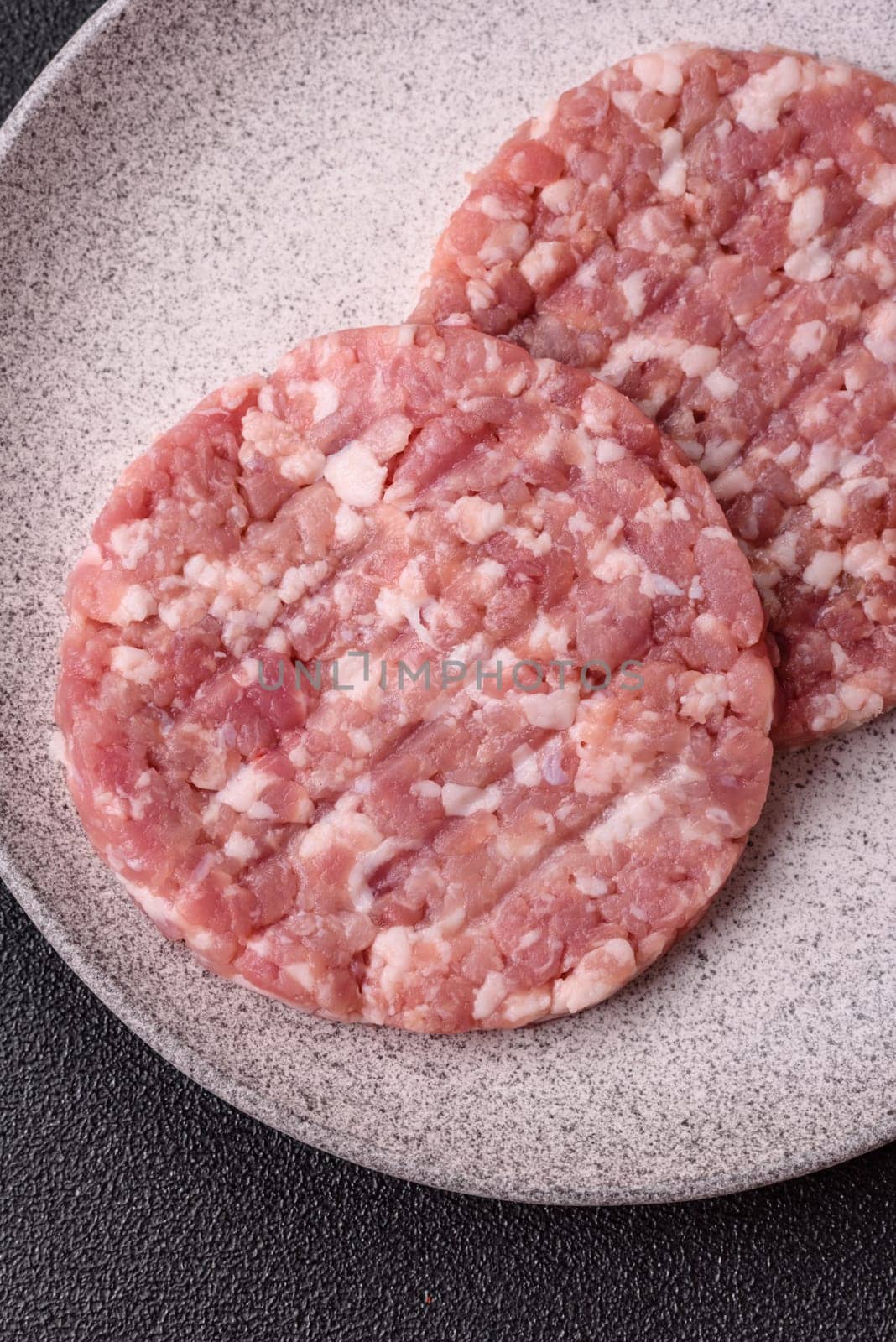 Fresh raw ground beef or pork burger patty with salt and spices on textured concrete background